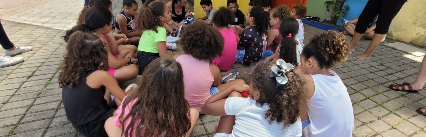 Imagem colorida de crianças sentadas no chão, am atividade com Carla Mauch, coordenadora da Mais Diferenças.
